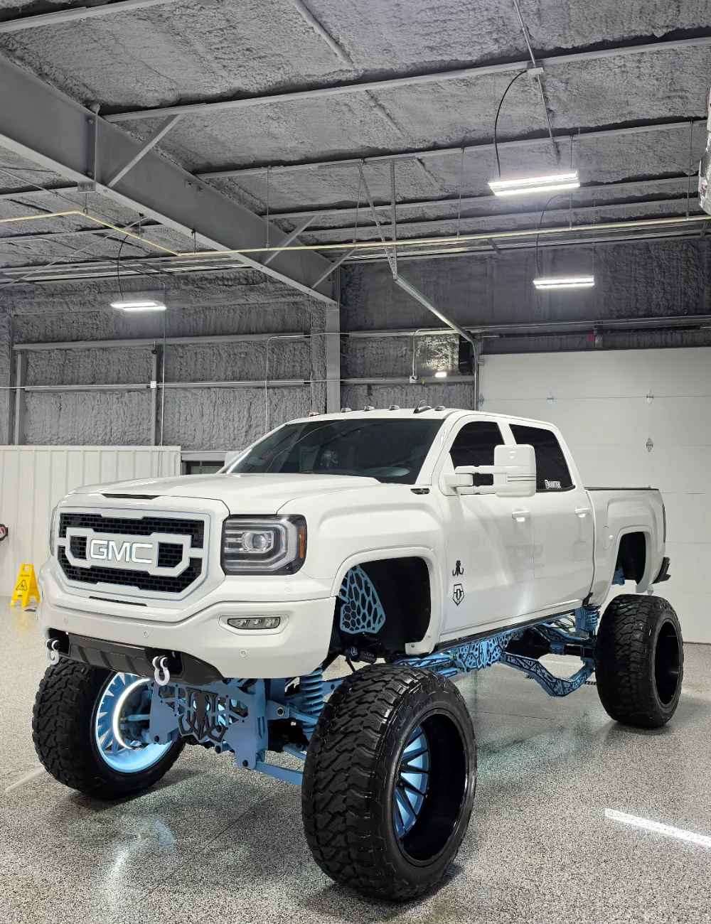 A lifted white GMC pickup inside the Detail Geex studio in Jacksonville