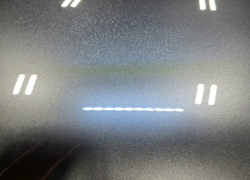 Dark metallic paint under inspection lighting, speckled with paint overspray