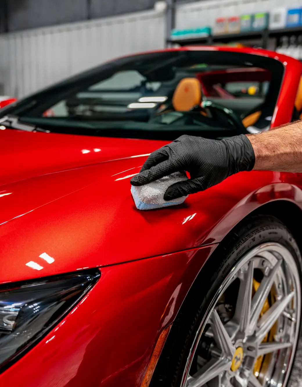 A gloved hand applying XPEL Fusion Plus ceramic coating to a red Ferrari fender