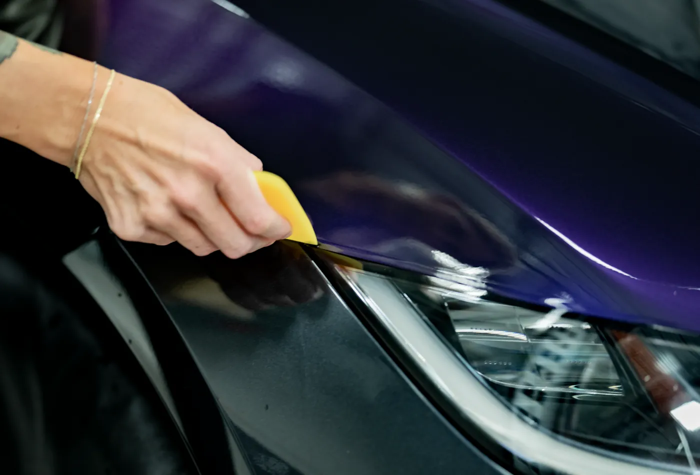 A hand squeegeeing purple XPEL color-change film down onto a fender