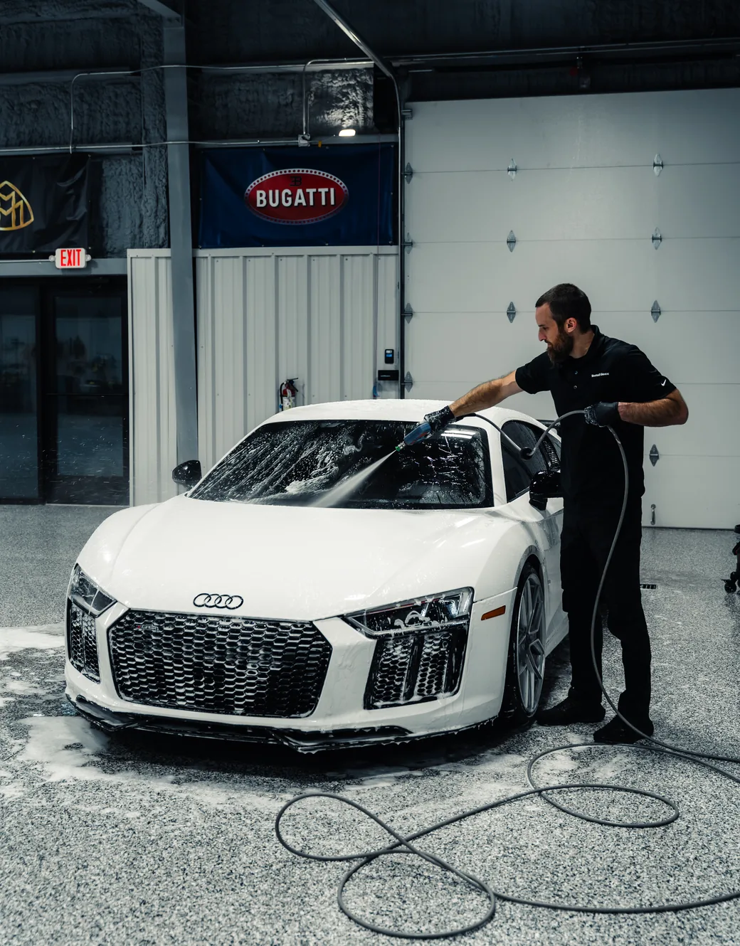 A white Audi R8 under a foam bath, being hand washed in the Detail Geex bay
