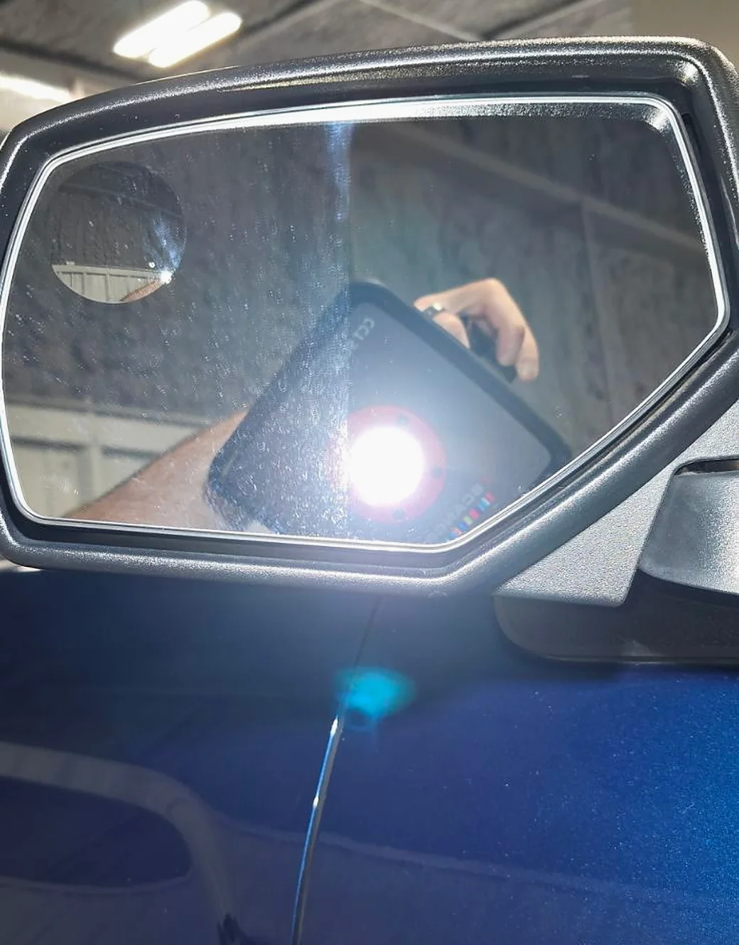 An inspection light held against a door mirror, showing water spotting