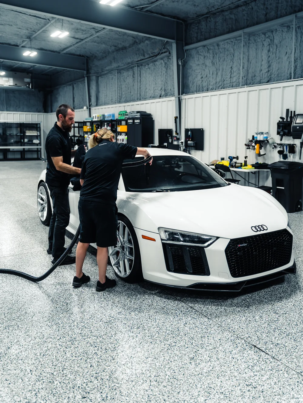 Two Detail Geex technicians working on a white Audi R8 in the bay
