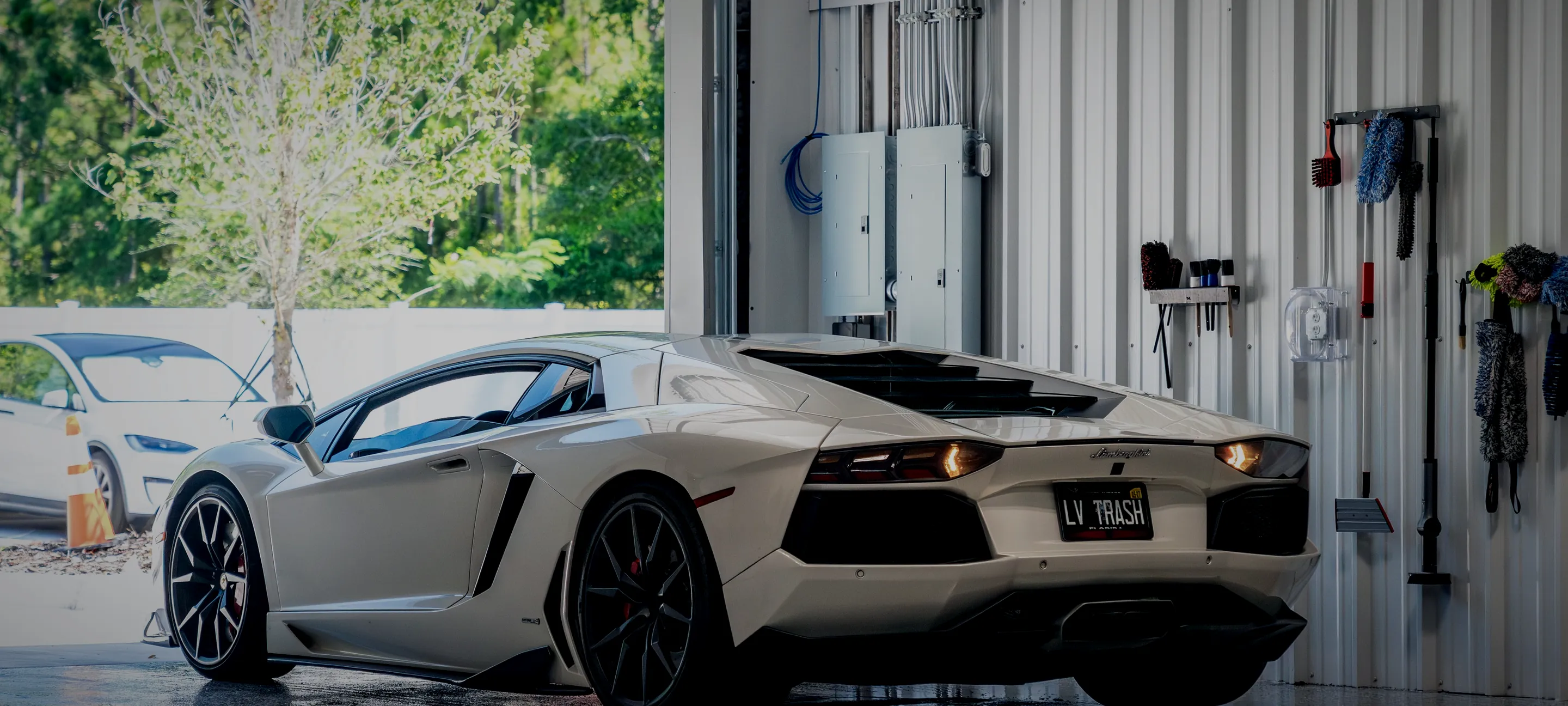 A white Lamborghini Aventador in the Detail Geex bay with the door open onto trees