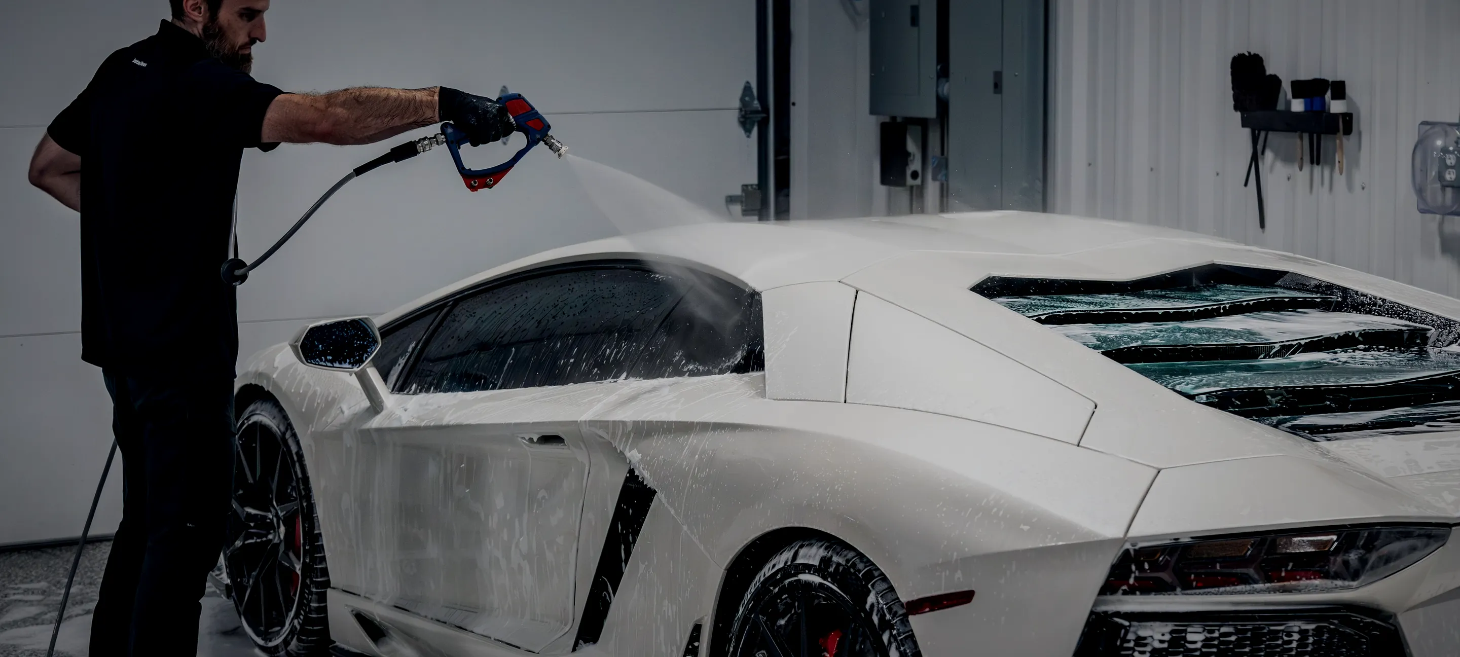A white Lamborghini Aventador under the foam lance inside the Detail Geex bay