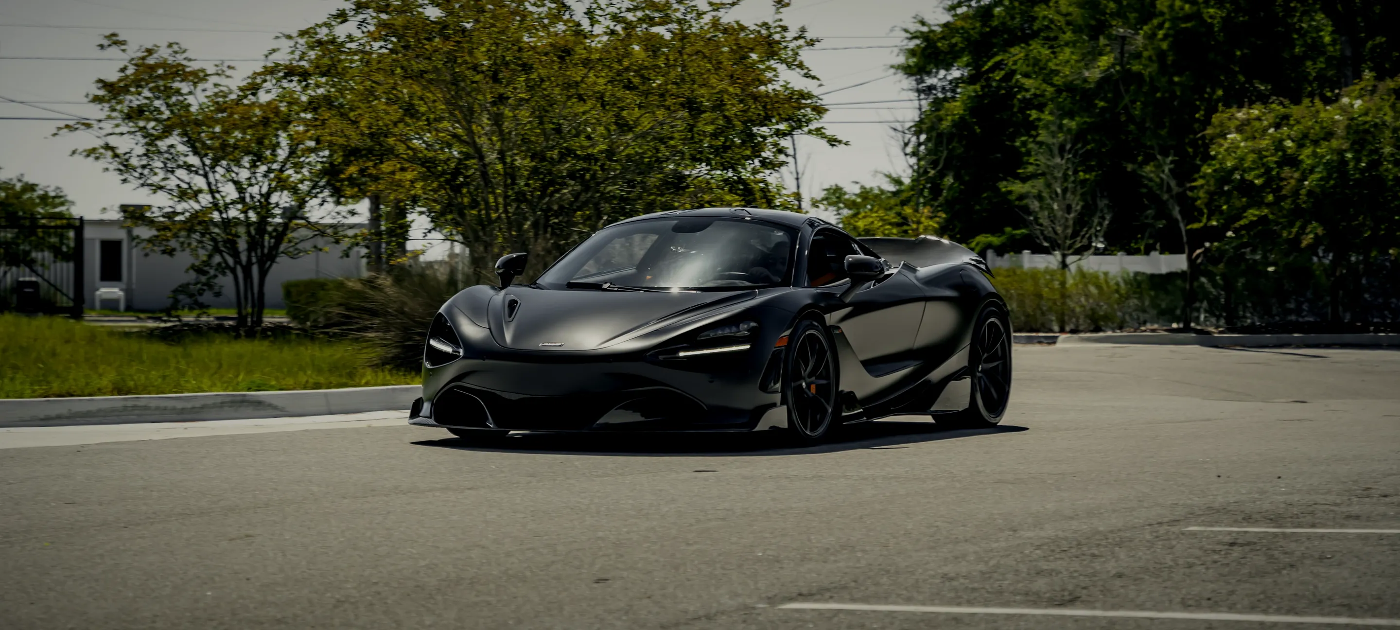 A black McLaren parked in the shade of trees outside