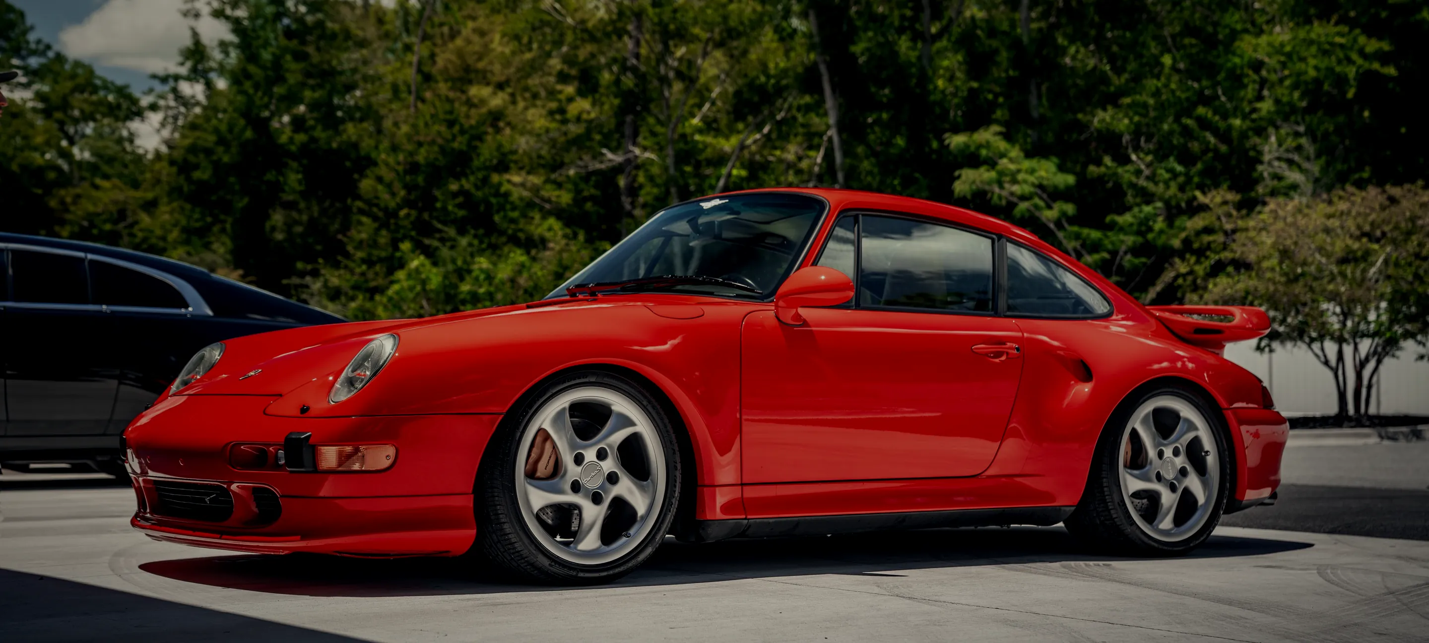 A red Porsche 911 parked on a tree-lined street near Neptune Beach