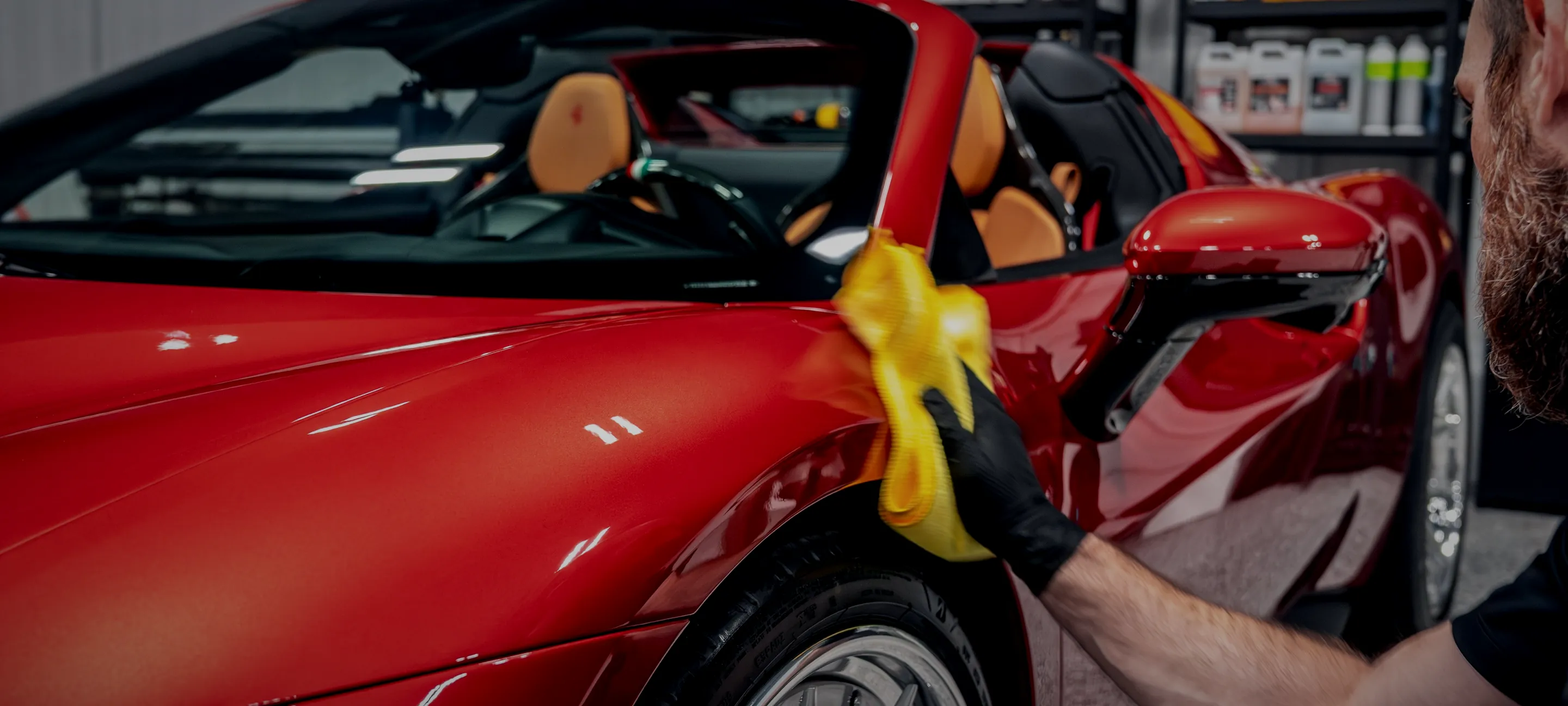 A technician working on the fender of a red Ferrari inside the Detail Geex studio