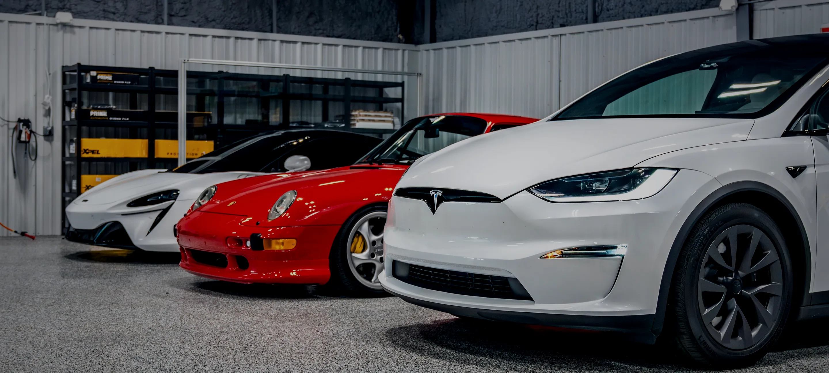 Exotic cars parked beside a daily-driven Tesla inside the Detail Geex bay