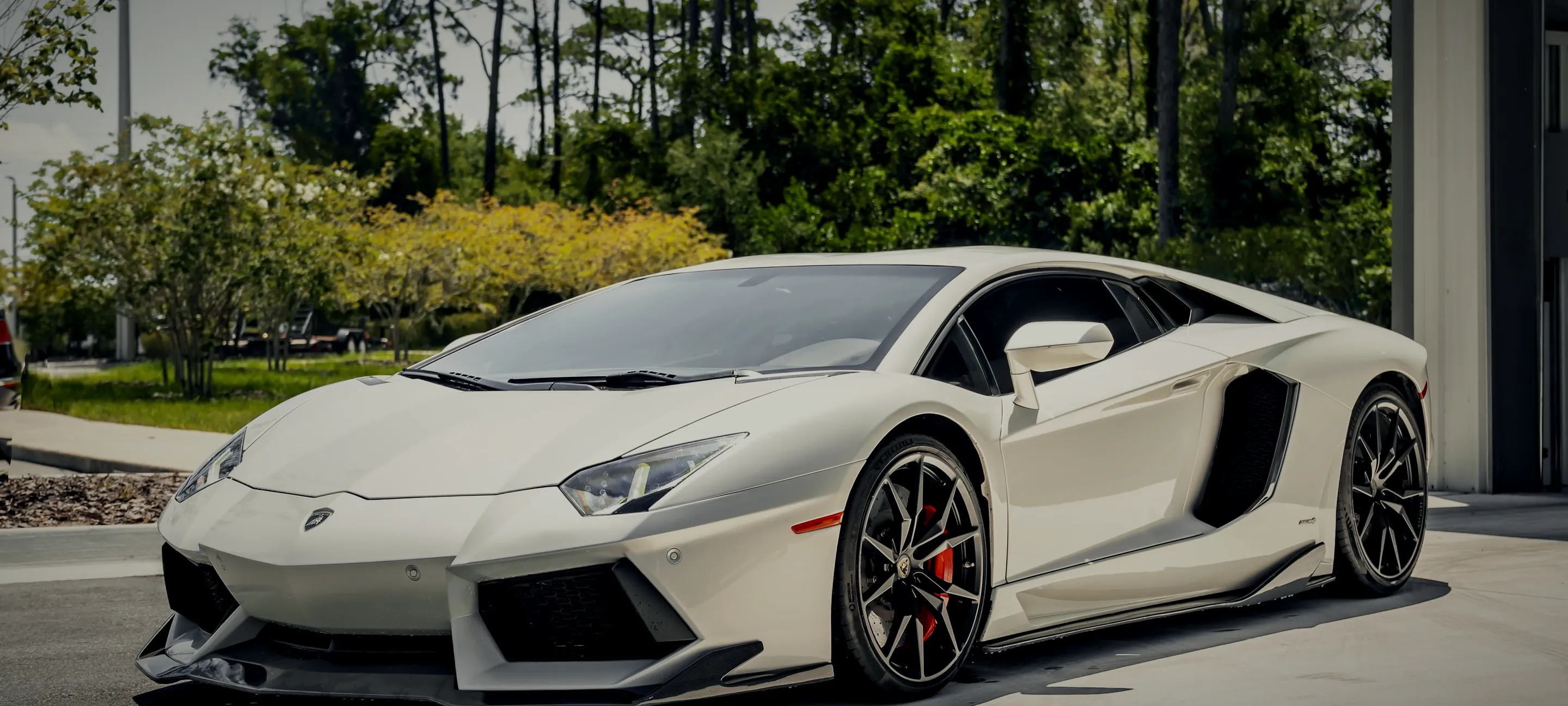 A white Lamborghini Aventador outside the Detail Geex studio among Florida pines