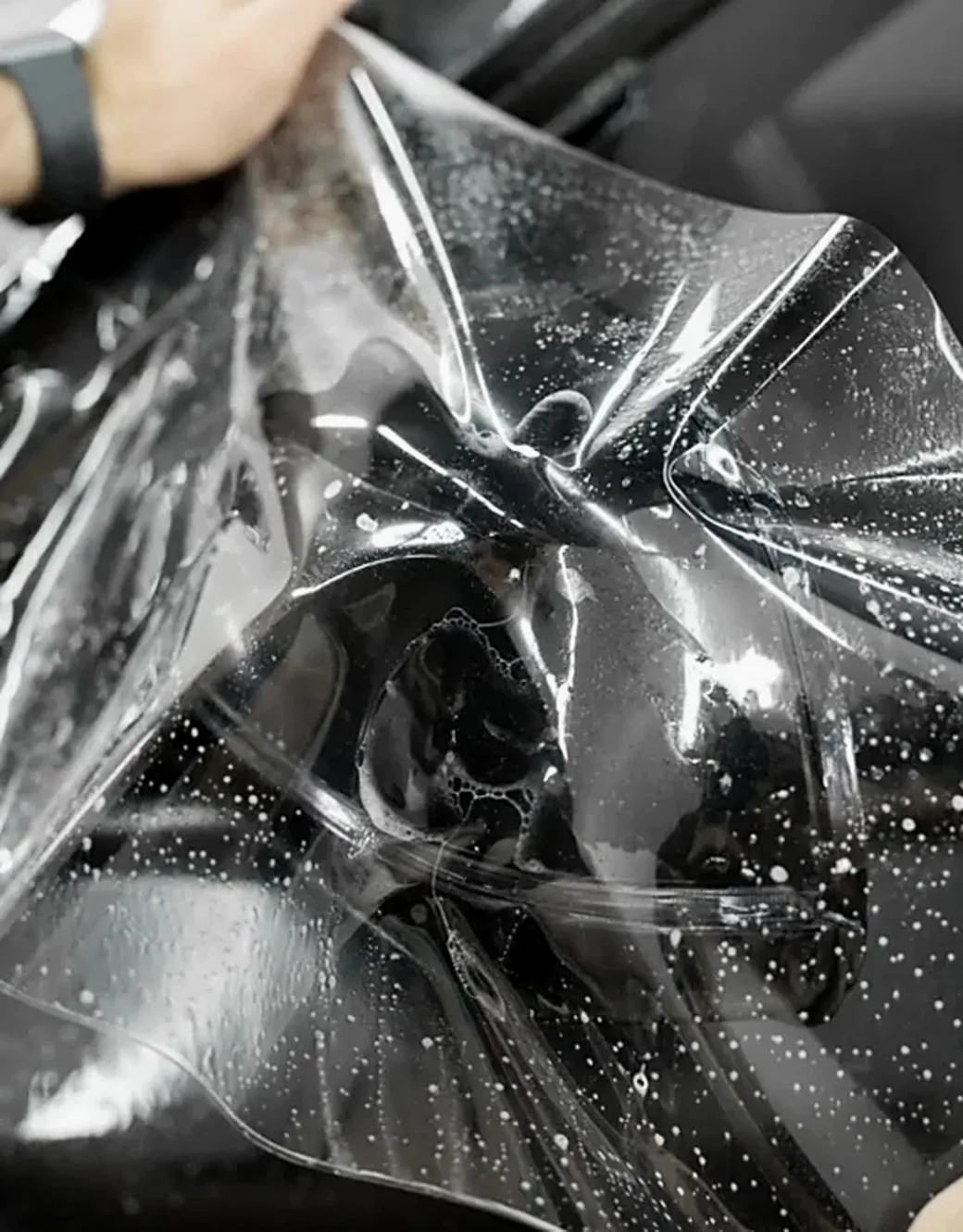Clear paint protection film being laid over a wet black body panel