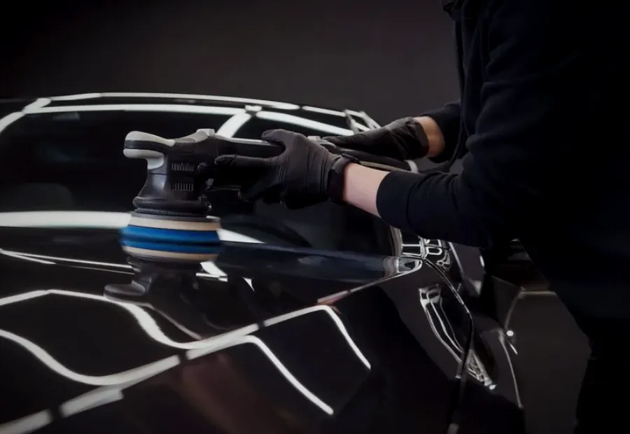 A dual-action polisher working a black hood under the studio lights