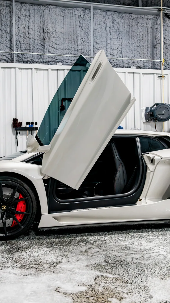 A white Lamborghini Aventador with its door up inside the Detail Geex studio