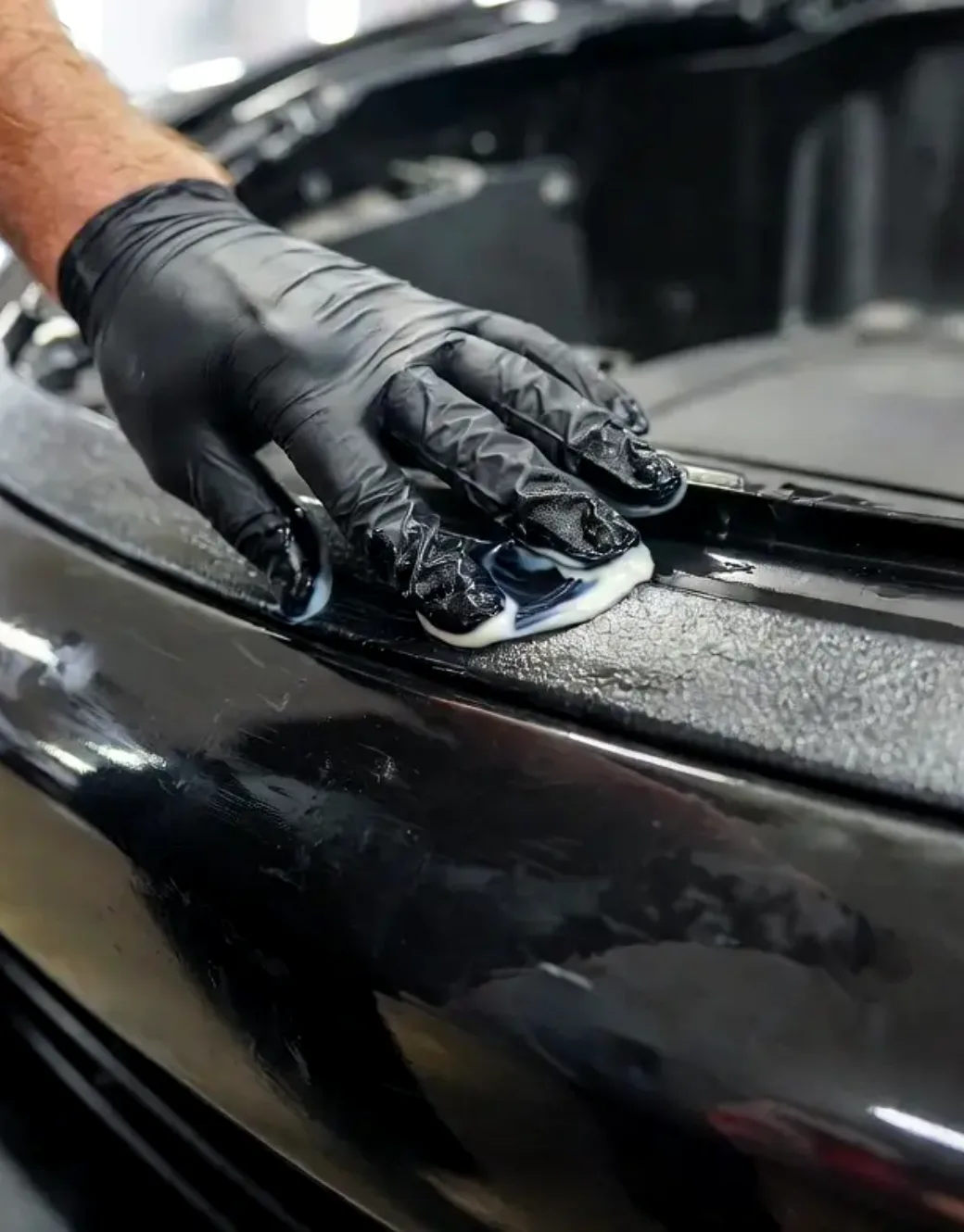 A gloved hand working black exterior trim back to a deep finish
